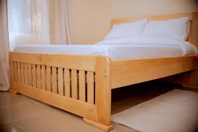 a wooden bed with white sheets and pillows on it at Tembo Homestay in Arusha