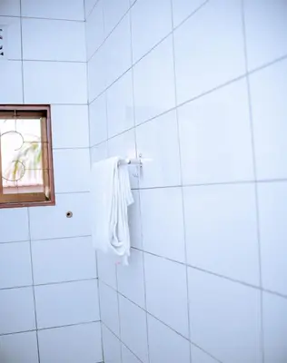 a white tiled bathroom with a window and a towel at Tembo Homestay in Arusha