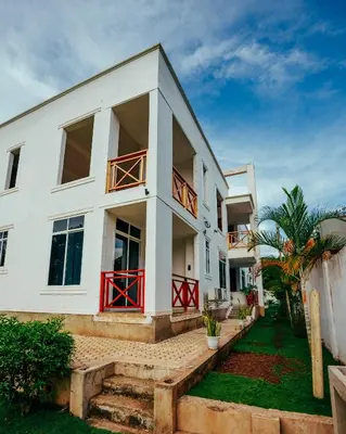 a white house with red doors and a yard at Shanti Apartments in Uru