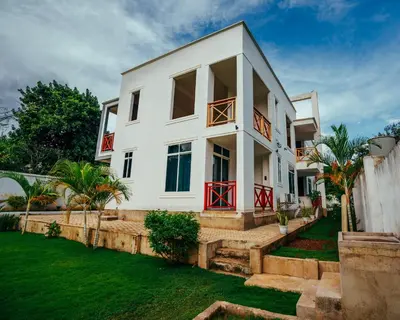 a white house with red doors and a yard at Shanti Apartments in Uru