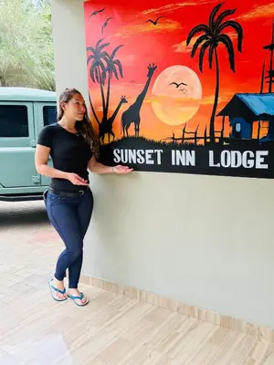 a woman leaning against a wall with a sunset inn lodge sign at Sunset Inn Lodge in Arusha