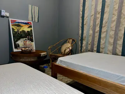 a bedroom with two beds and a chair and a table at Shambani Homestay in Moshi