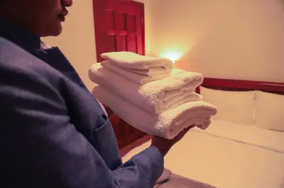 a woman holding a stack of towels in a room at River House Lodge International in Arusha