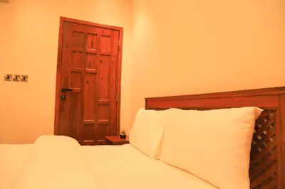 a bedroom with a bed with white sheets and a wooden door at River House Lodge International in Arusha