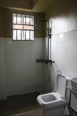 a bathroom with a toilet and a window at At Home Suites, Moshono Garden Arusha in Nkoanrua