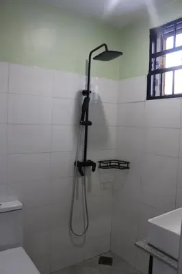 a shower in a white tiled bathroom with a shower head at At Home Suites, Moshono Garden Arusha in Nkoanrua