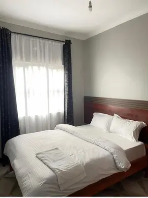 a bedroom with a bed with white sheets and a window at Kanyigo homes Apartments in Arusha