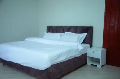 a large bed with white sheets and a night stand at Ngorongoro Gateway Homestay in Karatu