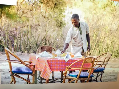 a man standing next to a table with a table cloth at Tindiga Tented Camp Eyasi in Mangola