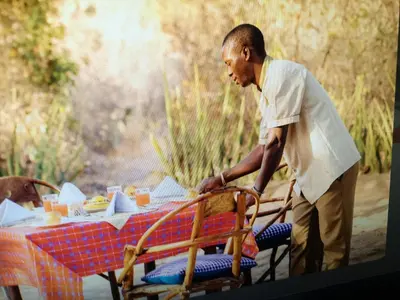 a man standing in front of a table with a chair at Tindiga Tented Camp Eyasi in Mangola