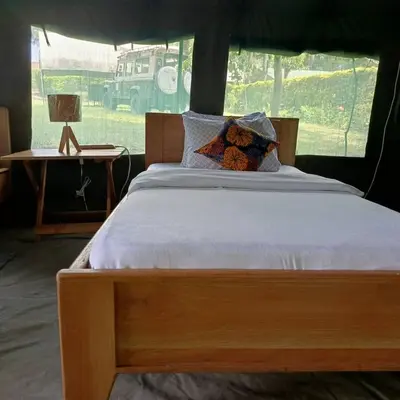 a wooden bed in a room with a table with a lamp at MCF LUXURY Tents in Moshi