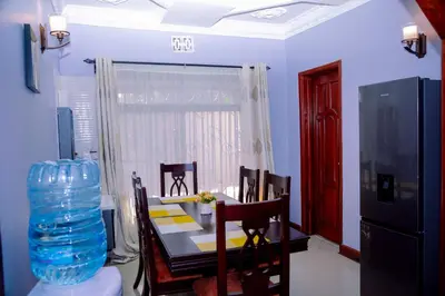 a dining room with a table and chairs and a water bottle at Hadraj Moshono Apartment1 in Arusha
