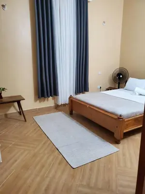 a bedroom with a bed and a table and curtains at Shilling Stay in Moshi
