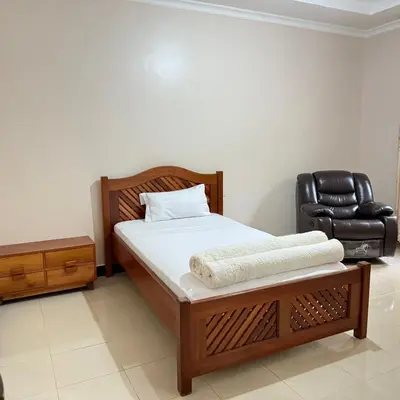 a bedroom with a bed and a leather chair at Mercy Apartments Moshi in Uru