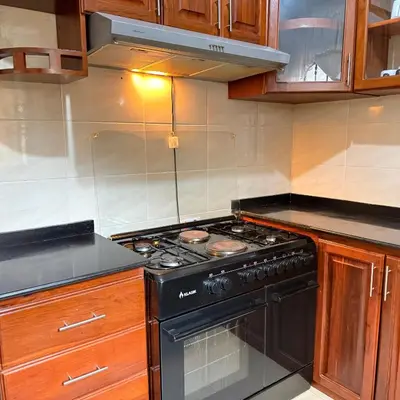 a kitchen with a black stove and wooden cabinets at Mercy Apartments Moshi in Uru