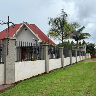 a fence in front of a house with palm trees at Mercy Apartments Moshi in Uru