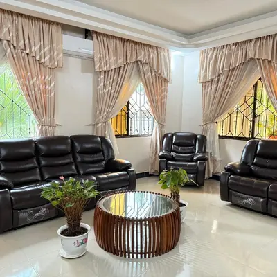 a living room with black leather furniture and windows at Mercy Apartments Moshi in Uru