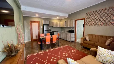 a living room with a couch and a table and a kitchen at Lush Garden Apartment in Arusha