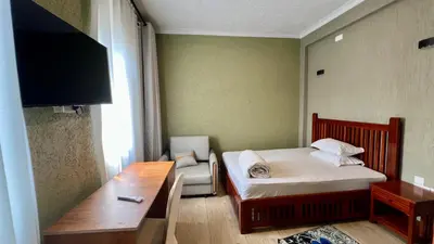 a small room with a bed and a desk and a television at Lush Garden Apartment in Arusha