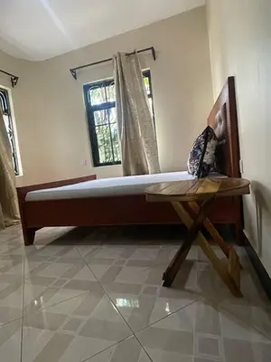 a bedroom with a bed and a table and a window at Abba's Homestay in Arusha