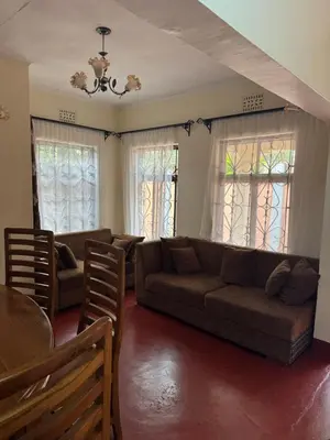 a living room with a couch and a table and windows at The Hut Hostel in Arusha