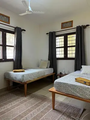 a bedroom with two beds and windows with curtains at Kivuli Lodge in Moshi