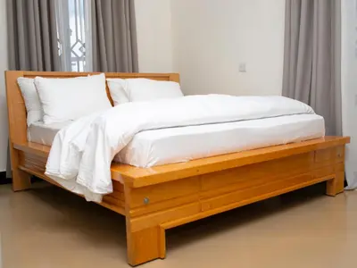a wooden bed with white sheets and pillows on it at damanda homes in Moshi