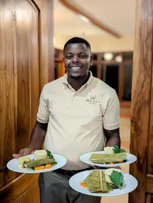 a man is holding two plates of food at Mvuli Mountain Lodge Ngorongoro in Karatu