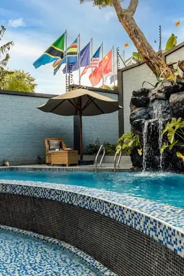 a swimming pool with an umbrella and flags at Shoki Shoki Lodge Arusha in Arusha