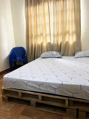 a bed in front of a window with a blue chair at 'La Maison' 2 bedroom house in Arusha in Arusha