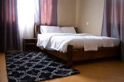 a bed with white sheets and a rug in a bedroom at Velam Home Stay in Arusha