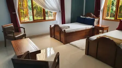 a bedroom with two beds and a chair and windows at Asante Karibu House in Arusha