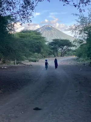 two people walking down a dirt road with a mountain in the background at Keremasi Camp Lake Natron in Mtowabaga