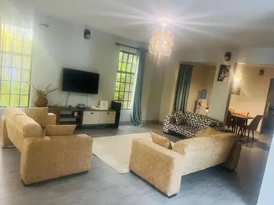 a living room with couches and a flat screen tv at Lively Cottages Momella,Main House in Usa River
