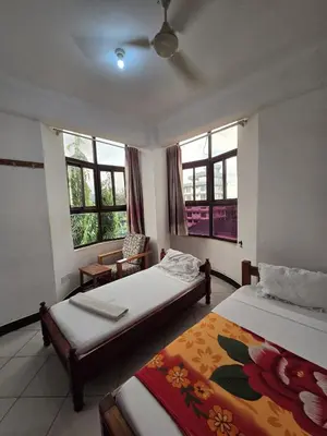 a bedroom with two beds and a chair and windows at Twiga Hotel - Tulivu Urban in Moshi