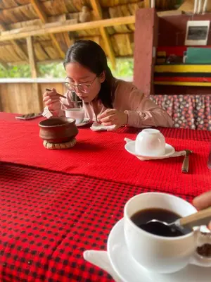 a woman sitting at a red table with a cup of coffee at Makahawani Farmhouse in Arusha