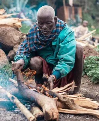 a man is sitting next to a fire at Emanyatta Lodge in Monduli