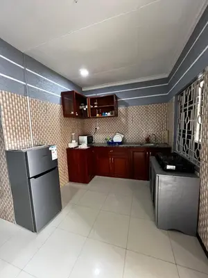 a kitchen with brown cabinets and a black refrigerator at Hadraj Sokokuu Apartment2 in Arusha