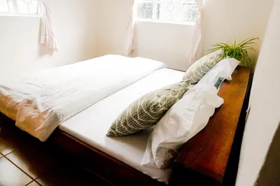 a bed with white sheets and pillows next to a window at Garden Villa Homestay in Arusha