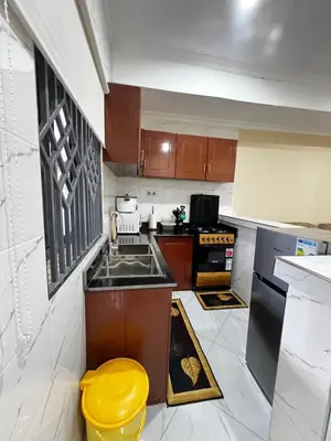 a kitchen with brown cabinets and a yellow stool at Hadraj Sokoine Apartment2 in Arusha