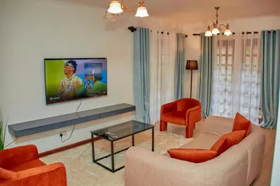 a living room with a couch and a tv on a wall at Fusion of Style & Comfort in Arusha