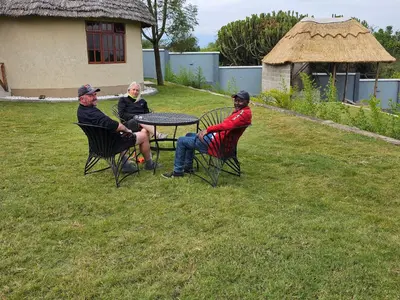 three people sitting at a table in a yard at Oiti Boma Lodge Arusha in Arusha