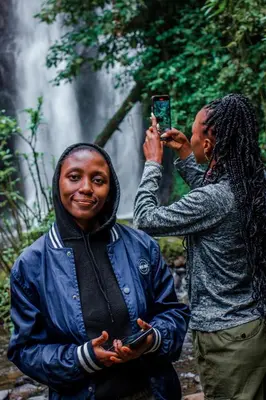 two people standing in front of a waterfall taking a picture at Avocado Kilimanjaro Homes in Marangu