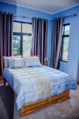 a bedroom with a bed with blue walls and windows at Avocado Kilimanjaro Homes in Marangu