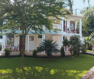 a large white house with trees in front of it at Hellens Riverside Villa Luxury Garden Room in Msaranga