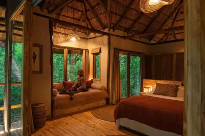 a woman sitting on a bed in a bedroom with windows at Koroi Forest Camp in Arusha