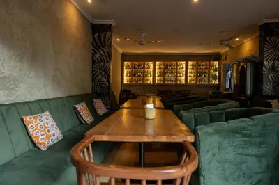 a restaurant with a wooden table and green couches at White House Hostels - Arusha in Arusha