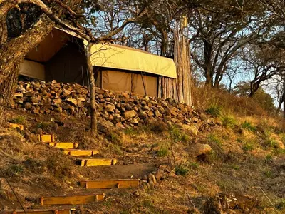 a building on a hill next to a rock wall at Namayana Camp in Makama
