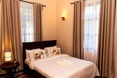 a bedroom with a bed with white sheets and a window at Neylisa Apartments in Arusha