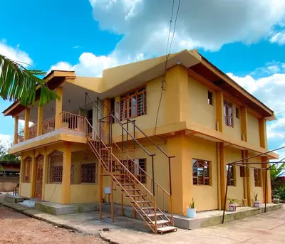 a yellow house with a staircase in front of it at Kinyaiya's Sereniry Farmstay